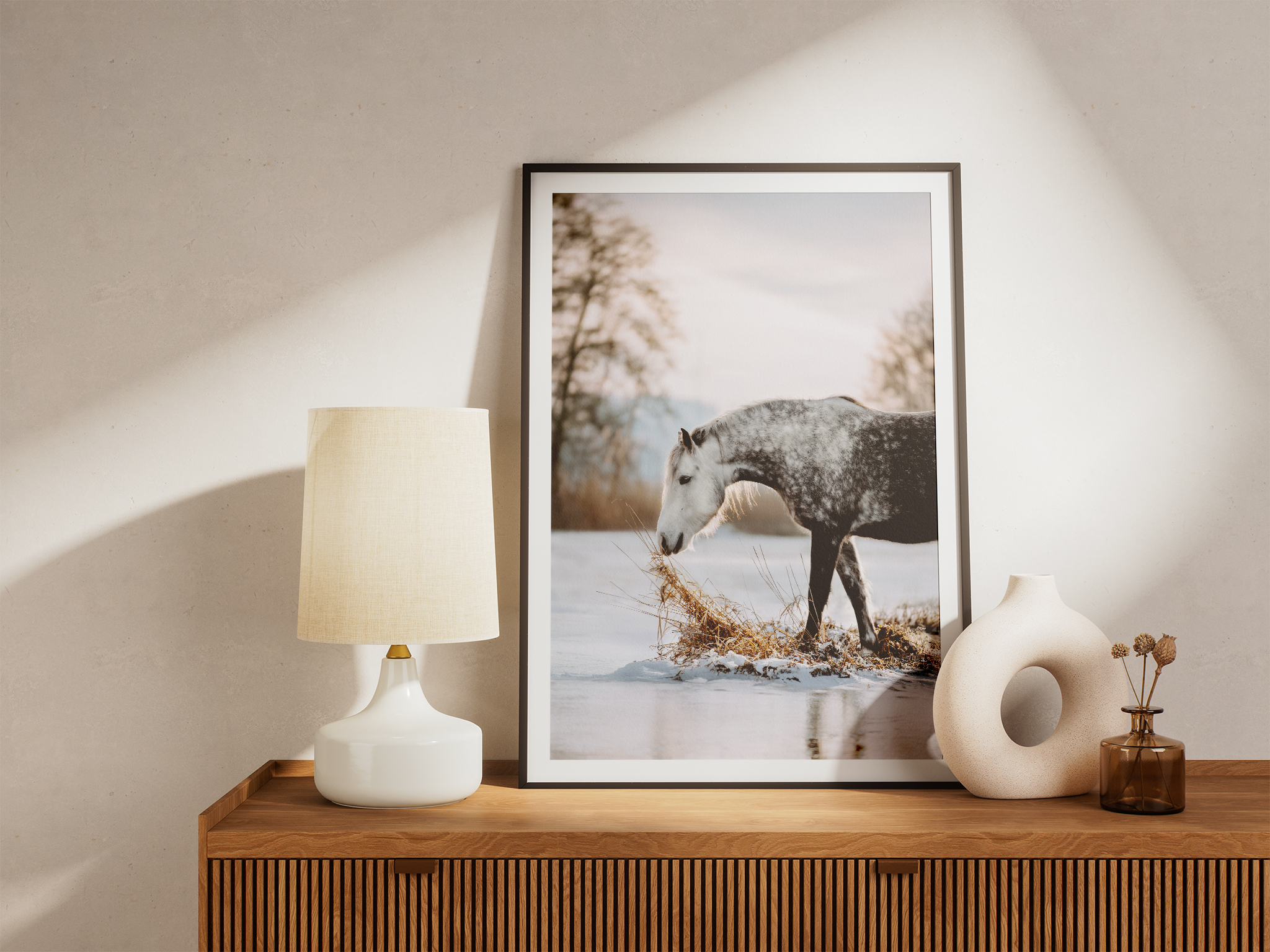 Fotoprint eines weißen Pferdes im Schnee, eingerahmt und stilvoll inszeniert auf einer Holzkommode mit Lampe und Vase im minimalistischen Wohnstil